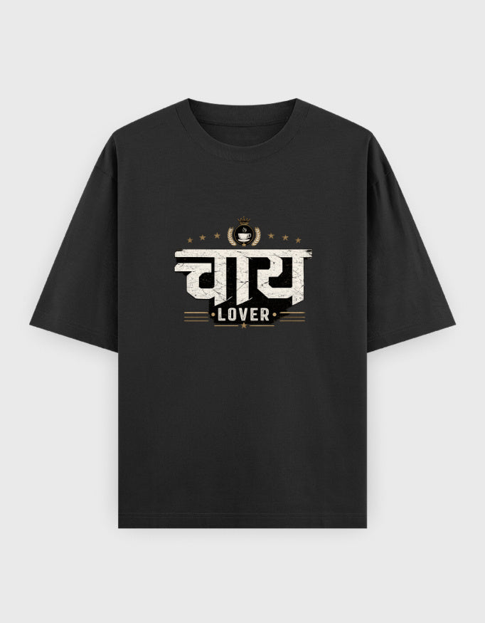 A black short-sleeve oversized t-shirt with a graphic print on the chest featuring the Hindi word 'चाय 
Lover' in white and gold, with 'LOVER' written below, displayed against a light gray background.