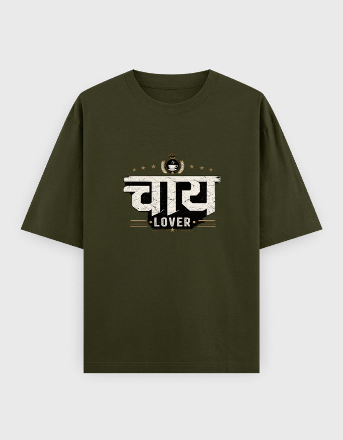 A black short-sleeve oversized t-shirt with a graphic print on the chest featuring the Hindi word 'चाय 
Lover' in white and gold, with 'LOVER' written below, displayed against a light gray background.