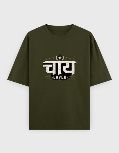 A black short-sleeve oversized t-shirt with a graphic print on the chest featuring the Hindi word 'चाय 
Lover' in white and gold, with 'LOVER' written below, displayed against a light gray background.