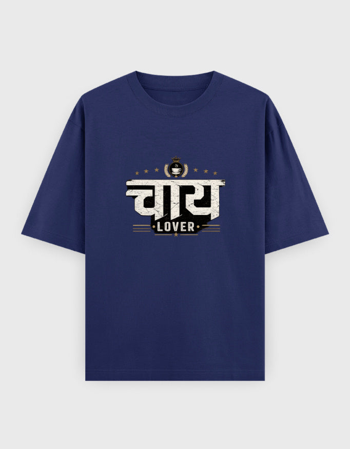 A navy blue short-sleeve oversized t-shirt with a graphic print on the chest featuring the Hindi word 'चाय 
Lover' in white and black, with the word 'LOVER' underneath and a small tea cup icon above, displayed on a light gray background.