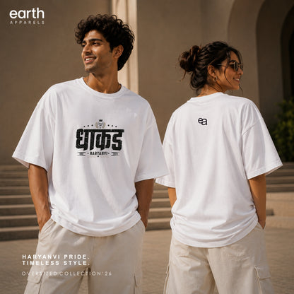 Two models wearing white Earth Apparel t-shirts in an outdoor architectural setting. The model on the left shows the front of the white oversized t-shirt with a black graphic print, and the model on the right shows the back of the white t-shirt with a small black logo.