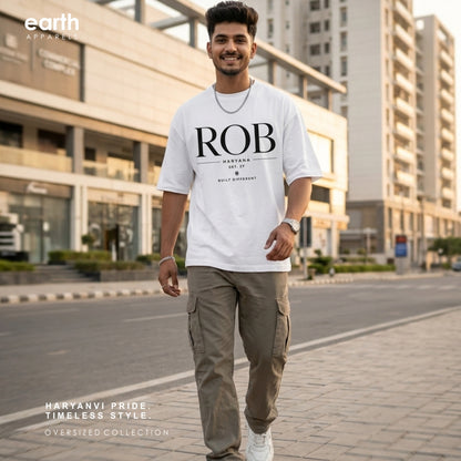 A man wearing an oversized white t-shirt with 'ROB' printed in black on the front, paired with khaki cargo pants and white sneakers, walking on a city street. The 'earth APPAREL' logo is visible in the top-left corner.