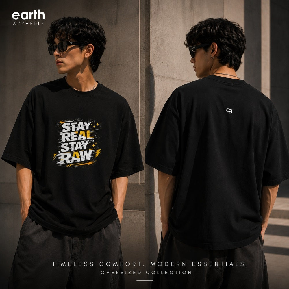 A model shown from the front and back wearing an oversized black t-shirt by Earth Apparel. The front features a graphic print with the text 'STAY REAL STAY RAW' in white and yellow, while the back has a small white logo.